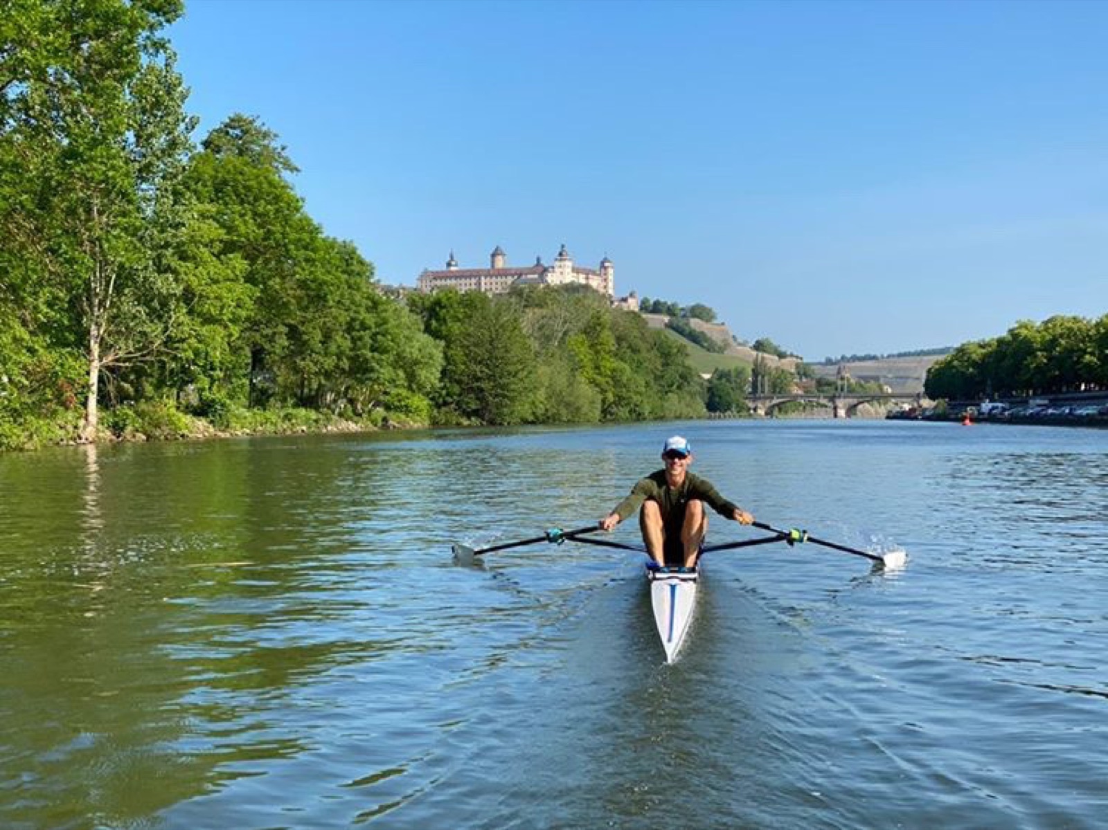 Finn rowing a single scull below a hilltop fortress in Germany